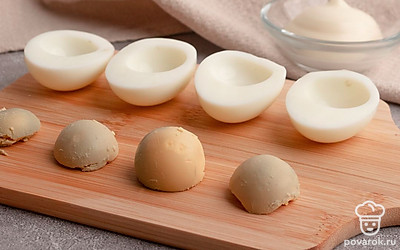 Вареные куриные яйца разрежьте пополам вдоль. Аккуратно отделите желтки от белков. Половинки белков отложите пока в сторону, а вареные яичные желтки разомните вилкой.