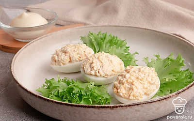 Наполните получившейся начинкой половинки яичных белков. Выложите закуску на листья свежего салата.