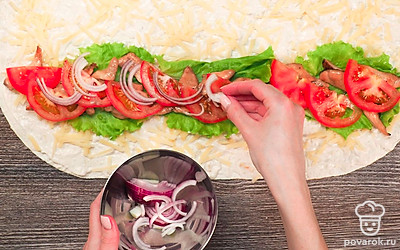 Соберите цезарь ролл по рецепту в домашних условиях. Разложите лист лаваша и хорошо промажьте его соусом. Посыпьте всю поверхность натертым сыром. С одного края полосами выложите салат, курицу, овощи. Сверните лаваш в рулет, не забывая подгибать края, чтобы начинка не высыпалась. Разогрейте сковороду и обжарьте без масла с двух сторон, чтобы сыр расплавился.