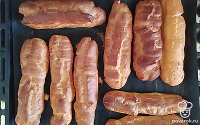 Переложить тесто в кондитерский шприц и отсадить 8 длинных эклеров (около 15 сантиметров) и 4 шарика. Поставить противни в заранее разогретую до 220 градусов духовку и выпекать 10 минут. После чего понизить температуру до 180 градусов и выпекать еще 30 минут. Готовые эклеры достать, сделать мелкие проколы, чтобы выпустить пар. Полностью остудить.
