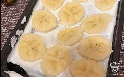 Смазываем его сметаной и распределяем нарезанные бананы.