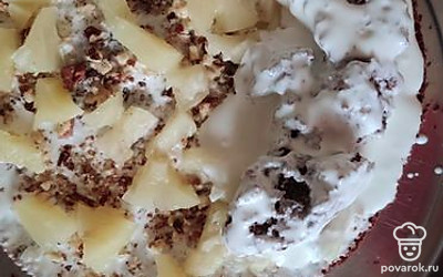 Разрезать корж пополам. Одну половину измельчить на куски. Сделать крем из сметаны и сахарной пудры. Обмазать корж кремом, посыпать ананасами и орехами.