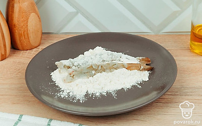 Обваляйте креветки в муке.