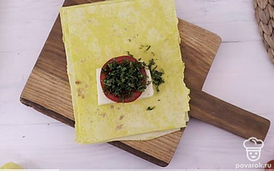 На каждый кусок лаваша выложите по одному ломтика сыра и помидора, добавьте измельченную зелень.