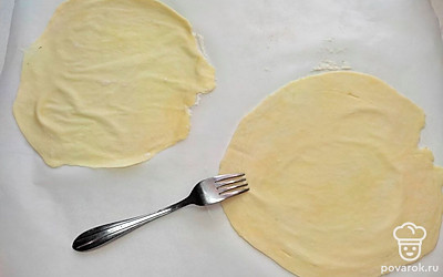 По истечении времени достаньте тесто из холодильника, разделите его на 10 мучных кружочков одинакового размера и каждый из них раскатайте в круглый пласт диаметром 20 см. Каждый мучной пласт проколите вилкой и отправьте корж на противень, застеленный пергаментом. Выпекайте коржи при температуре 250 °С в течение 15-20 минут до легкой румяности.