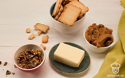 Заранее достаньте сливочное масло из холодильника. Мелко порубите грецкие орехи и раскрошите печенье.