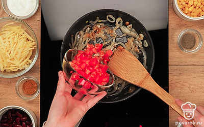 Приготовьте начинку. На разогретую сковороду налейте растительное масло и обжарьте чеснок с луком. Периодически помешивайте, жарьте 3-4 минуты на сильном огне. Выложите на сковороду порезанные помидоры и тушите 5 минут на среднем огне.