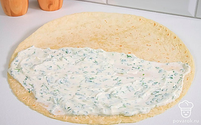 Разложите лист лаваша на столе. Намажьте половину листа сметаной с зеленью.