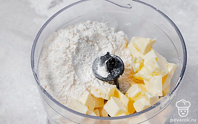 Насыпьте в чашу блендера муку. Нарежьте холодное масло на небольшие кусочки, добавьте его к муке. Хорошенько измельчите вместе.