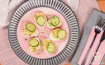 В каждое фаршированное яйцо аккуратно вставьте тонко порезанный ломтик огурца, сверху посыпьте мелко рубленой петрушкой.