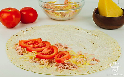 Выложите на лаваш начинку из сыра и колбасы, сверху положите нарезанный помидор.