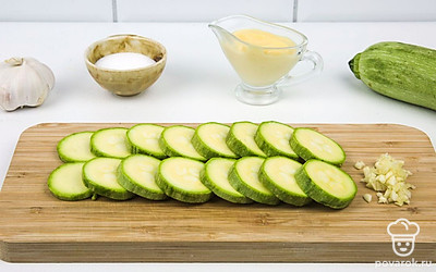 Кабачок нарежьте на равные кружочки по 1,5-2 сантиметра шириной. Мелко порубите чеснок.