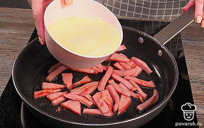 Приготовьте омлет. Залейте в сковороду с колбасой взбитые молоко и яйца, накройте крышкой и обжаривайте в течение 5-7 минут до готовности.