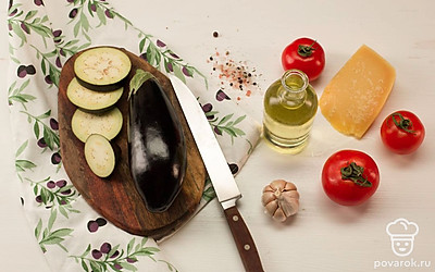 Баклажаны нарежьте кольцами и замочите на 20 минут в холодной воде с добавлением соли и сахара. Очистите чеснок, натрите пармезан на мелкой терке. Разогрейте духовку до 200°C. Подготовьте форму для запекания.