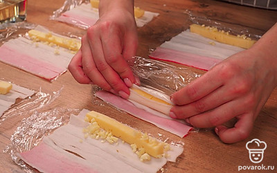 Сформируйте палочки. Аккуратно разверните крабовые палочки, чтобы они не развалились. Нарежьте сыр брусочками и заверните его в крабовые палочки. Сверху добавьте немного чеснока. У Вас должны получится крабовые рулетики.