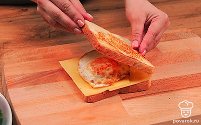 Соберите сэндвич. Для этого возьмите один ломтик хлеба, положите на него сыр и аккуратно выложите поджаренное яйцо. Сверху укройте вторым ломтиком хлеба.