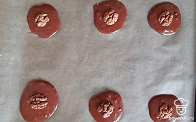 Распределите на противень тесто, оставляя место между печеньем, так как они увеличиваются примерно в два раза. Украсьте сверху орехами.