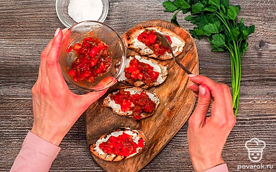 Тонким слоем намажьте творожный сыр. Сверху выложите теплую зажарку из томатов и чеснока, добавьте соль и перец.