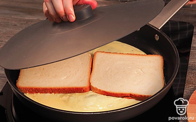 Соедините хлеб с омлетом. На жидкую массу выложите 2 ломтика хлеба. Накройте сковороду крышкой и дайте омлету схватиться. Жарьте 4-5 минут на слабом огне.