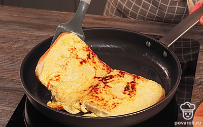 Обжарьте сэндвич с омлетом с обеих сторон. Аккуратно приподнимите омлет снизу широкой лопаткой и одним движением переверните на другую сторону. Накройте крышкой и обжарьте омлет на маленьком огне 3-4 минуты.