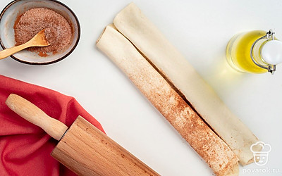 Подготовьте тесто. Раскатайте тесто в тонкий прямоугольный пласт. Смешайте сахар с корицей, половиной этой смеси присыпьте тесто. Сложите тесто от длинного края с двух сторон к центру. Посыпьте равномерно тесто оставшейся сахарной смесью и снова сложите тесто к центру. Прижмите получившиеся трубочки плотнее друг к другу.