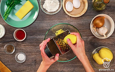 Подготовьте основу для картофельного теста. Для этого очищенный картофель натрите на крупной терке, выложите его в миску. Затем отожмите картофель.