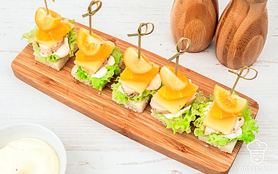 Сверху на курицу выложите сыр, дольки апельсина и помидоры черри. Проткните канапе шпажками.