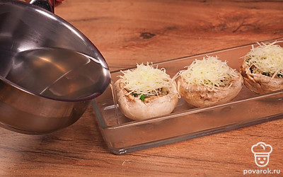 Шляпки грибов нафаршируйте подготовленной смесью, выложите на противень, посыпьте сверху сыром. На противень влейте 100-150 мл воды, в которой варились шампиньоны. Запекайте в духовке при температуре 180℃ 30 минут.