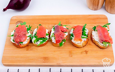 Намажьте на хлеб начинку из сыра и лука. Сверху выложите веточки рукколы. Следующим слоем уложите ломтики форели.