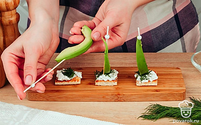 Следующим слоем накройте получившиеся бутерброды укропом. Почистите авокадо и нарежьте его на кусочки. Каждый ломтик авокадо следует нанизывать на шпажку и соединить с хлебом.