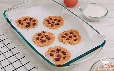 Застелите противень пергаментной бумагой. Сформируйте печенье и выложите на противень. Сверху выложите кусочки шоколада.