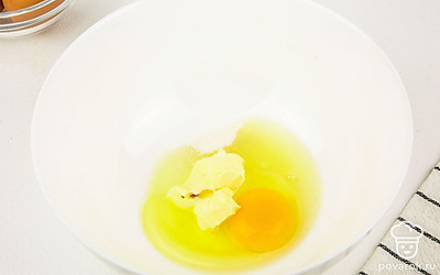 Возьмите глубокую миску, разбейте в нее яйцо и добавьте размягченное сливочное масло.