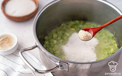 Всыпьте в кастрюлю с крыжовником и лимоном белый и желирующий сахар. Тщательно перемешайте массу, чтобы сахар начал растворяться.