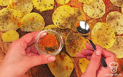 Подготовьте картофель. Нарежьте ножом картофель на тонкие пластины толщиной до 2 мм. Залейте слайсы водой и промойте, чтобы избавиться от крахмала. Излишки влаги уберите бумажным полотенцем. Выложите картофельные кружки в один слой на доску и посыпьте солью и смесью специй.