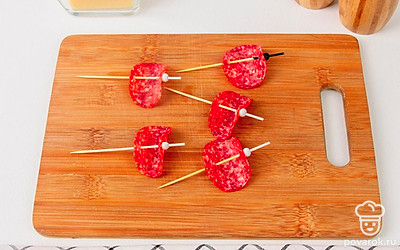 Проткните помидорку черри насквозь и подвиньте ее вплотную к ломтику колбасы (но не сжимайте “парус”).