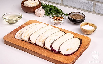 Отрежьте плодоножку баклажана и нарежьте его вдоль ломтиками толщиной 5 мм. Положите нарезанный баклажан в миску и посыпьте солью. Аккуратно руками распределите соль по ломтикам. Отставьте баклажан в сторону на 20 минут. Соль вытянет лишнюю горечь из баклажанов.