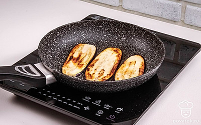 После того, как баклажаны, присыпанные солью, постоят, из них выделится сок. Отожмите слегка баклажаны, чтобы удалить лишнюю влагу. Разогрейте сковороду, влейте растительное масло и обжарьте ломтики на среднем огне по 2 минуты с каждой стороны.