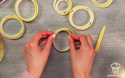 Сформируйте луково-сырные колечки. Делать это лучше на пергаментной бумаге. На лист пергаментной бумаги выложите луковые кольца: сначала большое, а внутрь положите поменьше. Между кольцами поместите полоски сыра, чтобы не осталось промежутков.