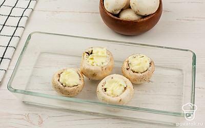 Смешайте чеснок со сливочным сыром, по желанию добавьте молотый перец. Полученной смесью начините шампиньоны. Переложите грибы в противень для запекания, предварительно смазанный небольшим количеством растительного масла.