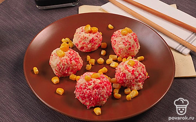 Готовые шарики из крабовых палочек с плавленым сыром выложите на сервировочное блюдо, украсьте зернами консервированной кукурузы.