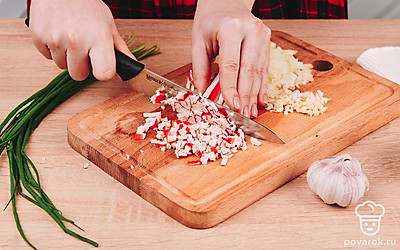 Крабовые палочки нарежьте небольшим кубиком и отправьте в миску к луку и чесноку.