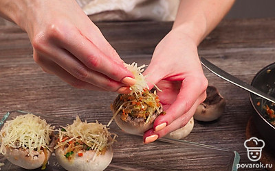 Запеките грибы. Начините шляпки грибов подготовленной начинкой. Насыпьте сверху оставшийся сыр. Переложите в форму для выпекания и поставьте в духовку, разогретую до 190 градусов, на 25 минут.