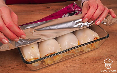 Приготовьте фаршированных кальмаров. Начините тушки кальмаров начинкой. Переложите в форму для выпекания, накройте фольгой. Отправьте в разогретую до 150 градусов духовку на 15 минут.