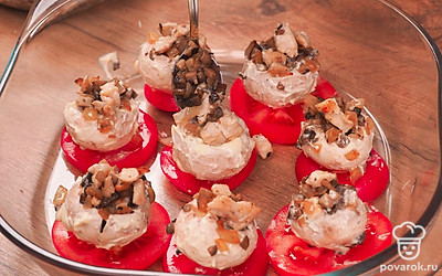 В форму для запекания уложите ломтики помидоров. На каждый ломтик положите шляпку. На дно шляпки поместите по кусочку сливочного масла. Нафаршируйте шампиньоны начинкой из лука, чеснока, курицы и ножек грибов. Сверху посыпьте сыром. Запекайте грибы с начинкой в духовке 30-35 минут при температуре 180℃.