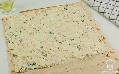 Расстелите на столе лаваш и размажьте по всей его поверхности начинку, оставляя внизу отступ 5 см.