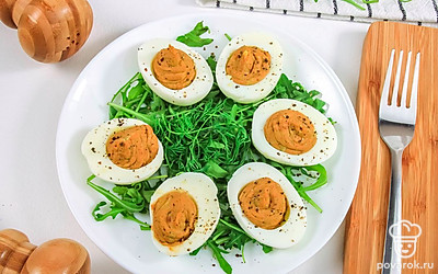 Выложите фаршированные яйца на «подушку» из зелени и украсьте черным молотым перцем. Готово.
