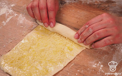 Сформируйте хлебные палочки. Каждому кусочку придайте прямоугольную форму толщиной 2-3 мм. Смажьте маслом с чесноком, посыпьте тертым сыром. Скатайте в плотный рулетик. Затем растяните их в жгутики. Скрутите каждую заготовку в спираль.