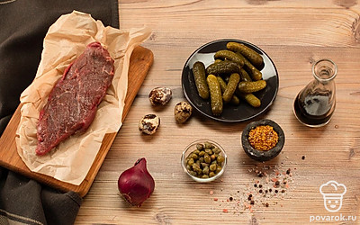 Говядину нарежьте мелкими кубиками. Незадолго до начала приготовления слегка заморозьте говядину, чтобы было проще нарезать ее. Измельчите каперсы и корнишоны. Нарежьте лук очень мелкими кубиками.