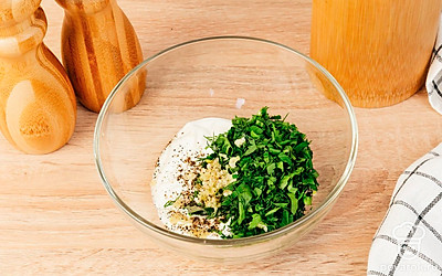 Выложите сметану в миску, добавьте в неё нарубленную зелень, выдавите туда же 1-2 зубчика чеснока, поперчите и посолите по вкусу. Аккуратно размешайте соус, равномерно распределив зелень и специи.