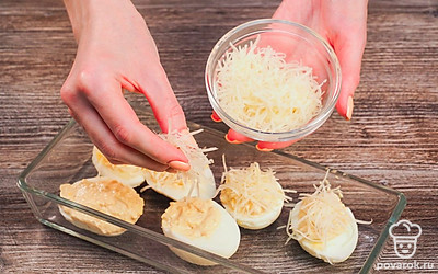 Нафаршируйте и запеките яйца. При помощи чайной ложки равномерно заполните белковую часть яиц начинкой. Сверху выложите натертый сыр, положите яйца на противень и отправьте в разогретую до 150 градусов духовку отправьте на 5 минут.